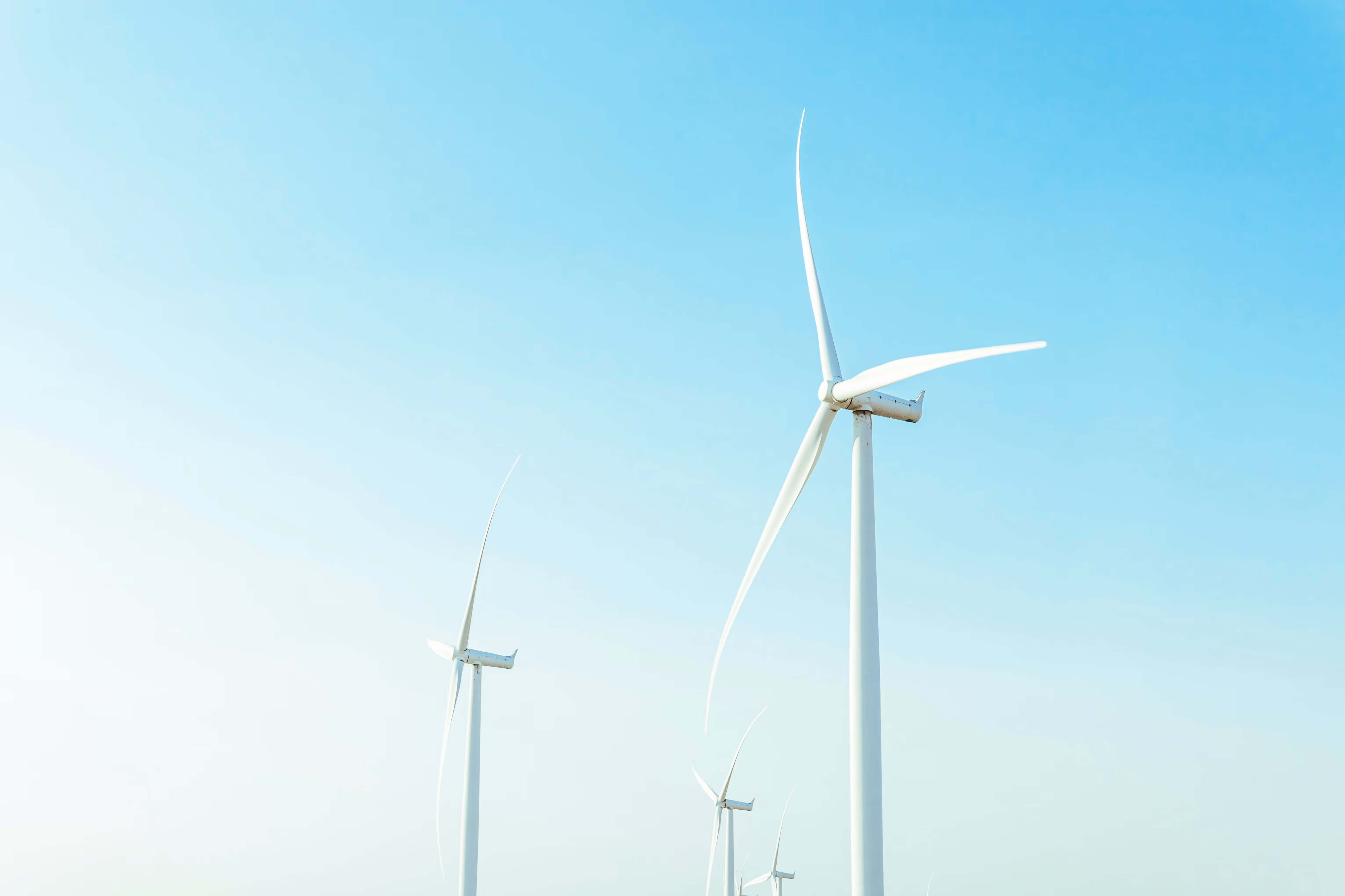 Several white wind turbines standing against a clear blue sky.