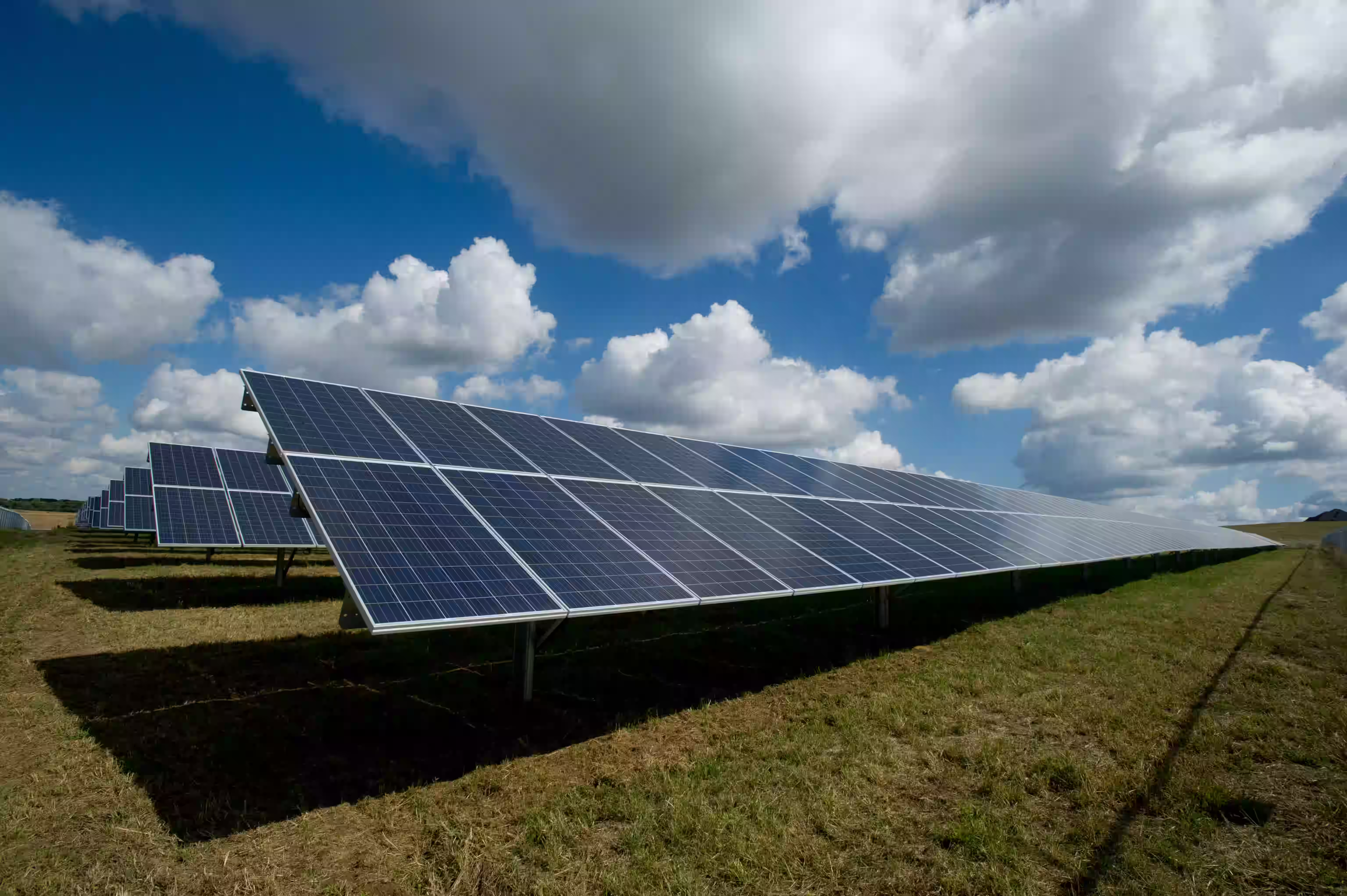 Rows of solar panels installed on a grassy field under a partly cloudy blue sky.